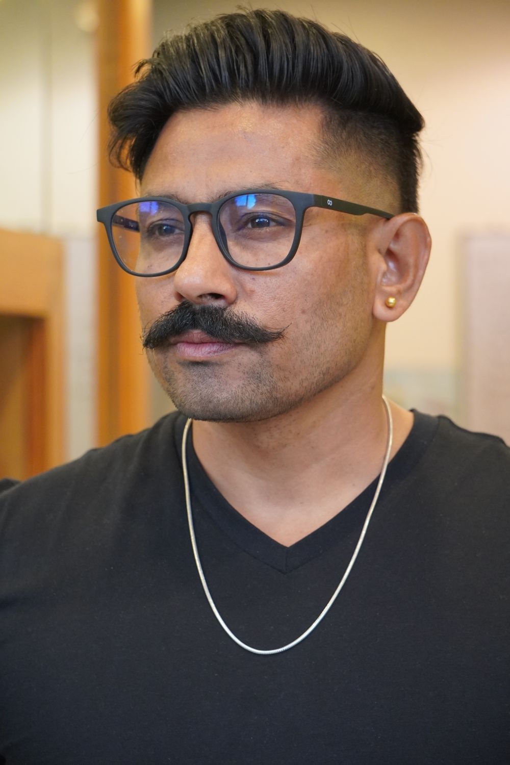 man wearing glasses with a textured short quiff and mustache
