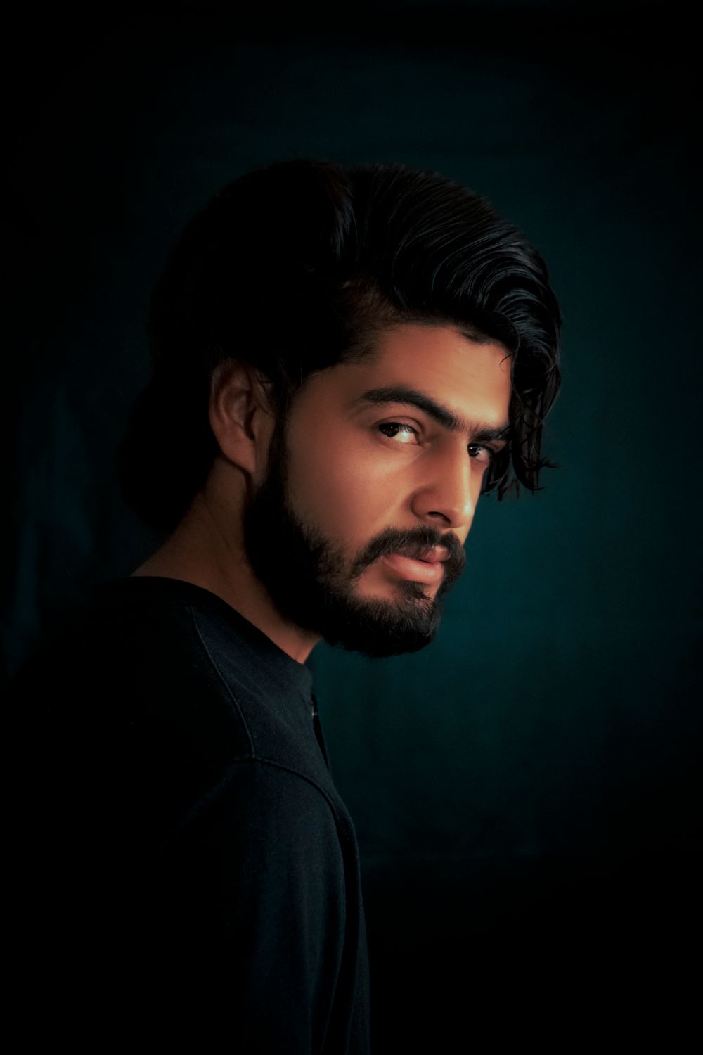 bearded man with medium wavy hair in a dark studio portrait